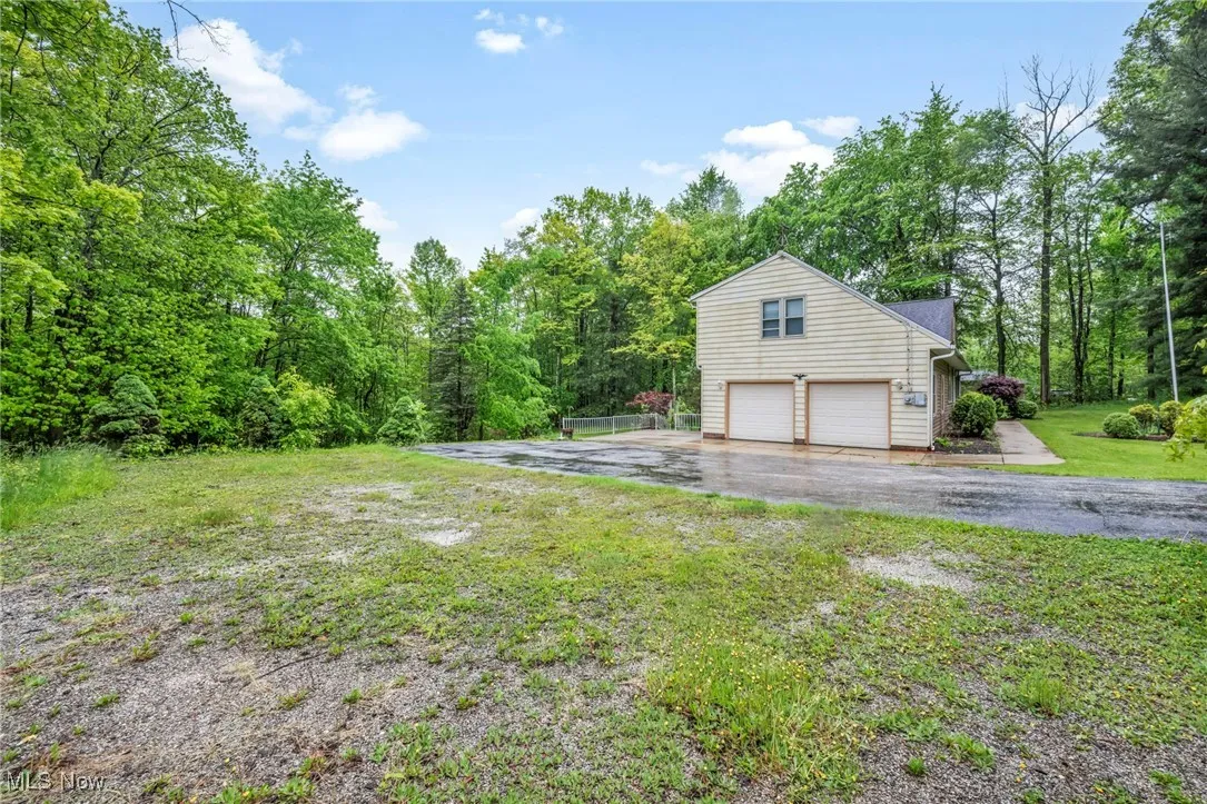 View of grassy yard with driveway, a garage, and a wooded view