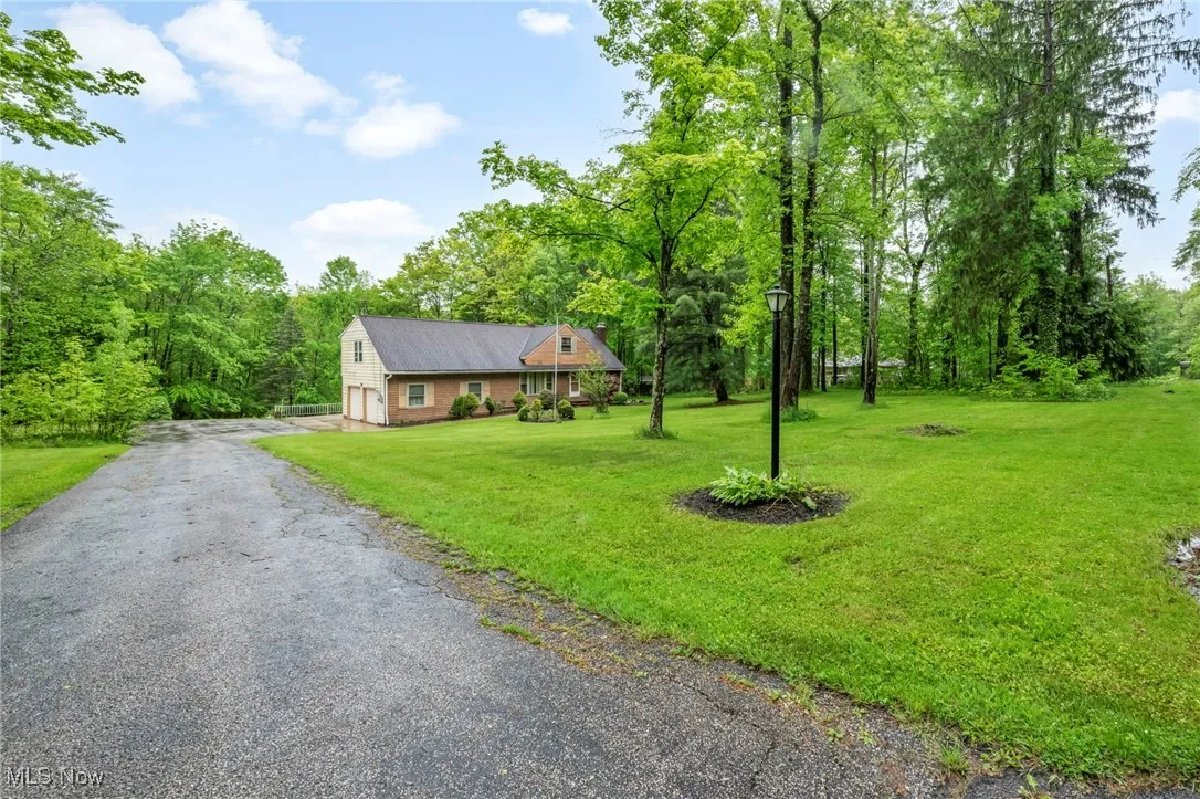 View of front facade with asphalt driveway, a front lawn, a view of trees, and a garage