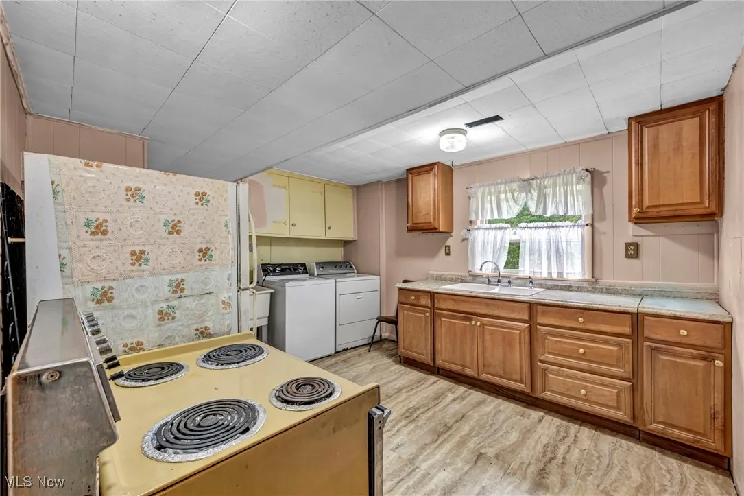 Kitchen with a sink, white range with electric cooktop, independent washer and dryer, light wood-style flooring, and light countertops