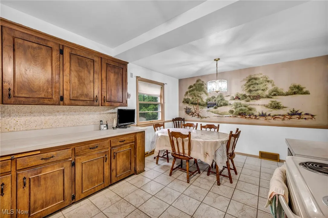 Kitchen featuring white electric range oven, a chandelier, light countertops, hanging light fixtures, and brown cabinetry