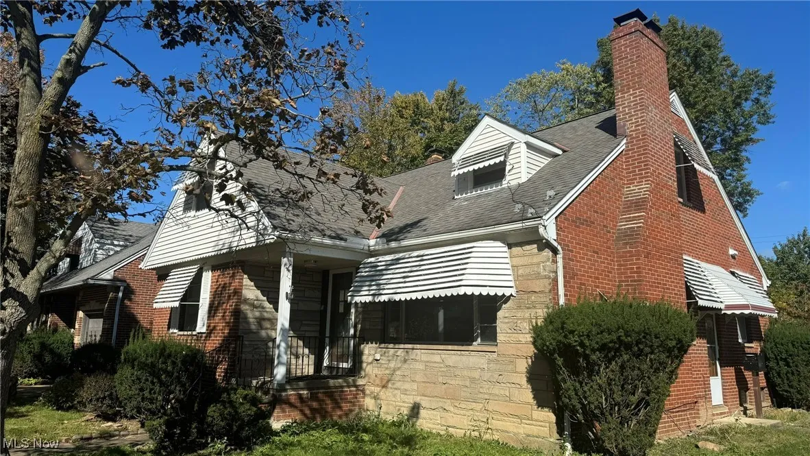 View of front facade featuring a chimney, brick siding, and roof with shingles