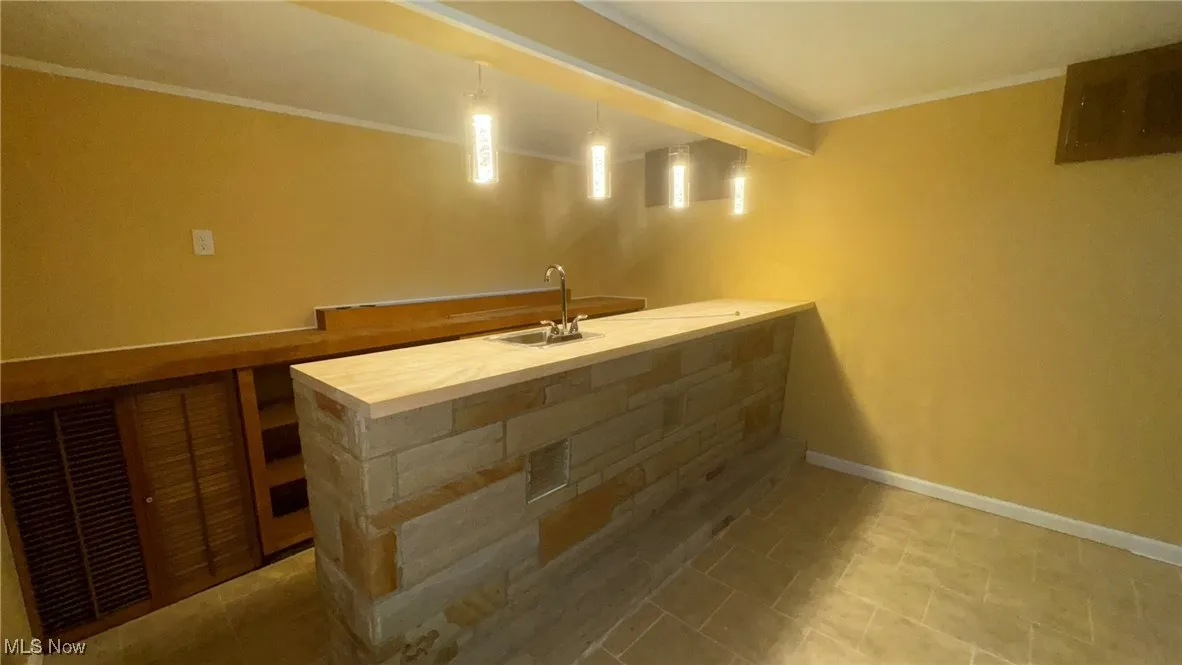 Indoor wet bar with baseboards, crown molding, and hanging light fixtures