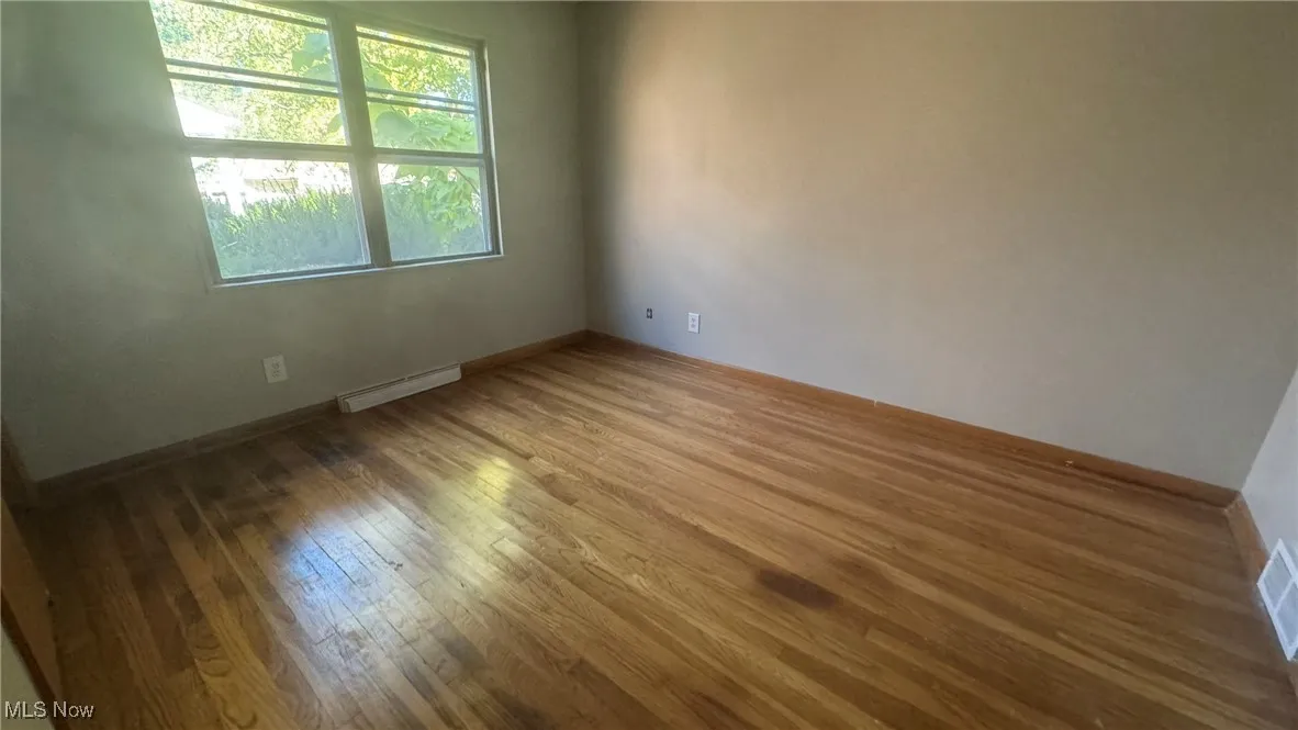 Spare room with wood finished floors, a baseboard heating unit, and baseboards