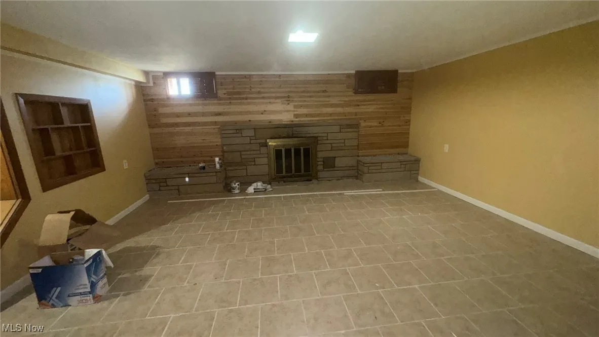 Unfurnished living room with wooden walls, a stone fireplace, baseboards, and built in shelves
