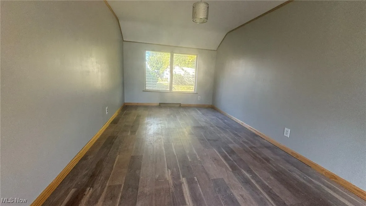 Empty room with dark wood-style floors, vaulted ceiling, and baseboards