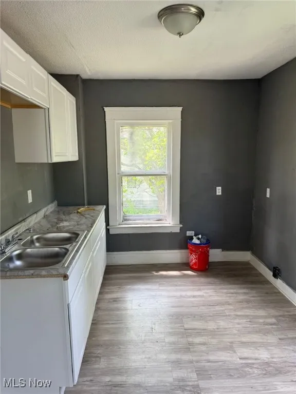 Kitchen featuring a sink, white cabinets, baseboards, and light wood finished floors