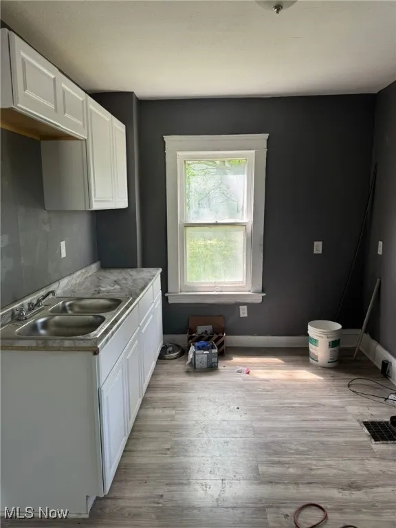 Kitchen with a sink, white cabinetry, light wood-style floors, and light countertops