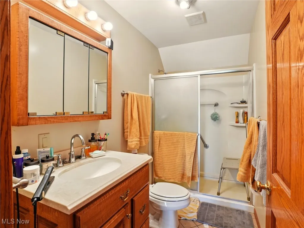 Full bath featuring vanity, a stall shower, toilet, vaulted ceiling, and tile patterned floors