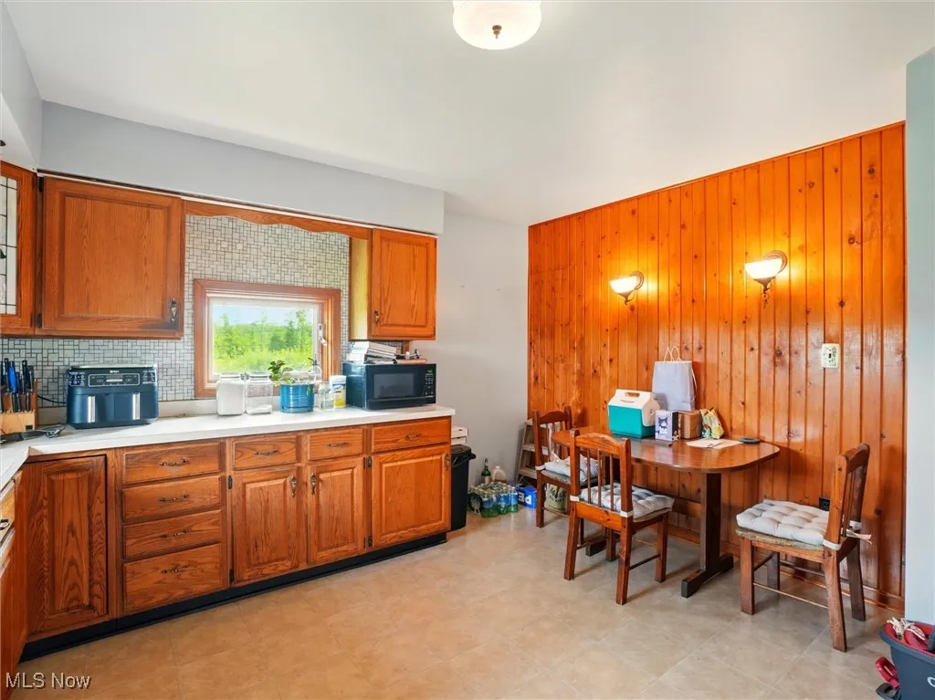 Kitchen with black microwave, brown cabinets, wood walls, light countertops, and tasteful backsplash