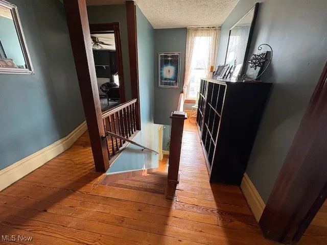 Hallway featuring an upstairs landing, a textured ceiling, wood-type flooring, and baseboards