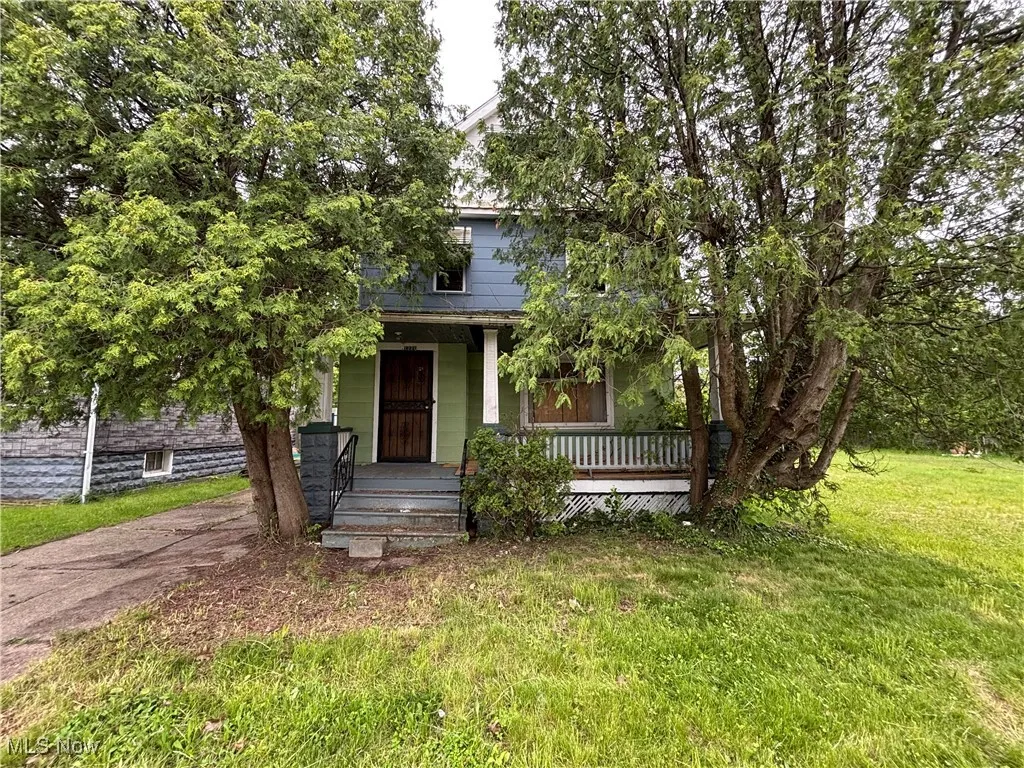 View of property hidden behind natural elements with a porch and a front yard