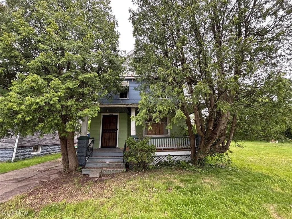 View of property hidden behind natural elements featuring covered porch and a front yard