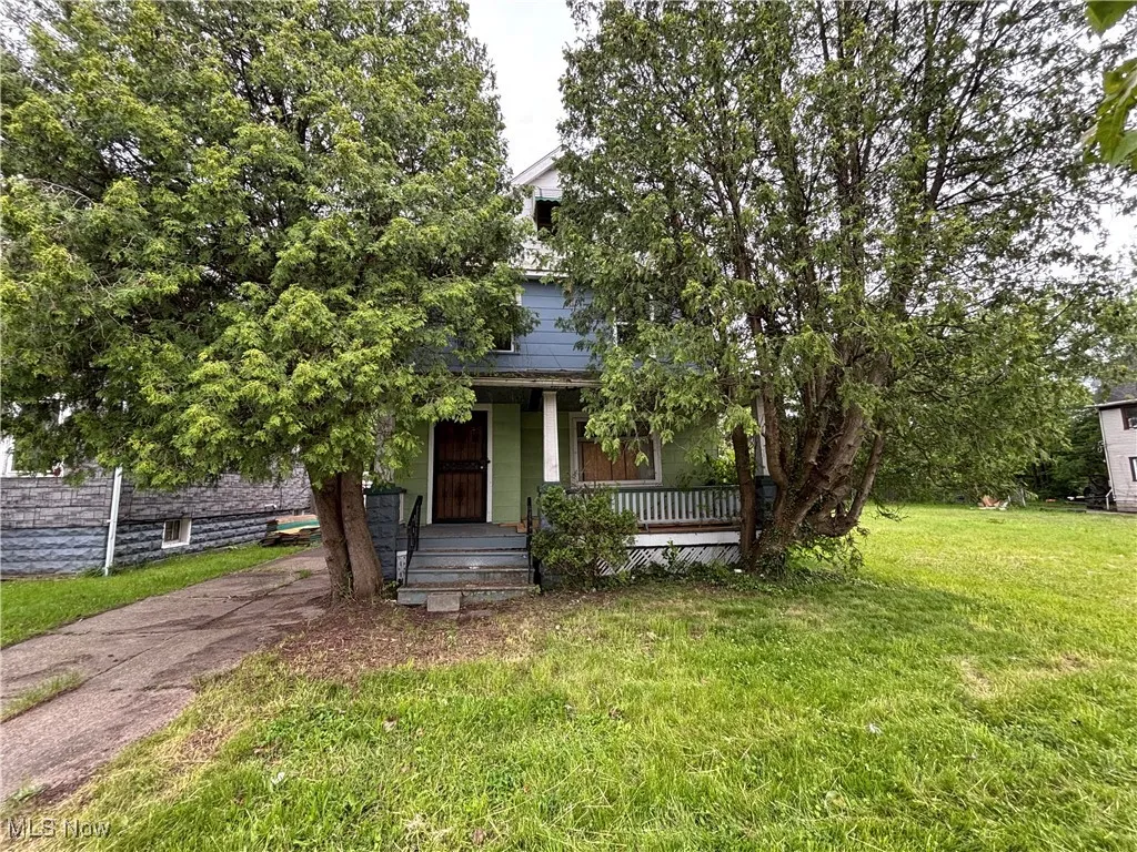 View of property hidden behind natural elements with covered porch and a front yard