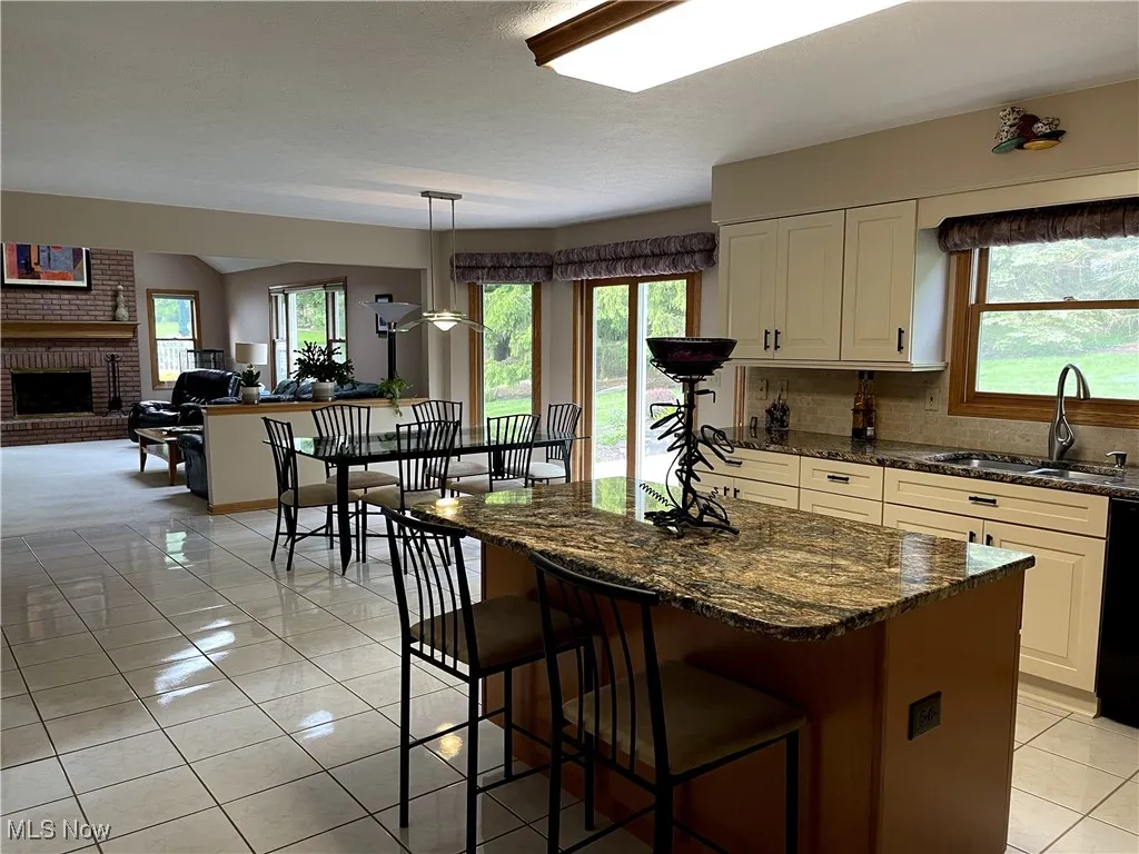 Kitchen featuring a sink, a fireplace, tasteful backsplash, white cabinets, and a kitchen bar
