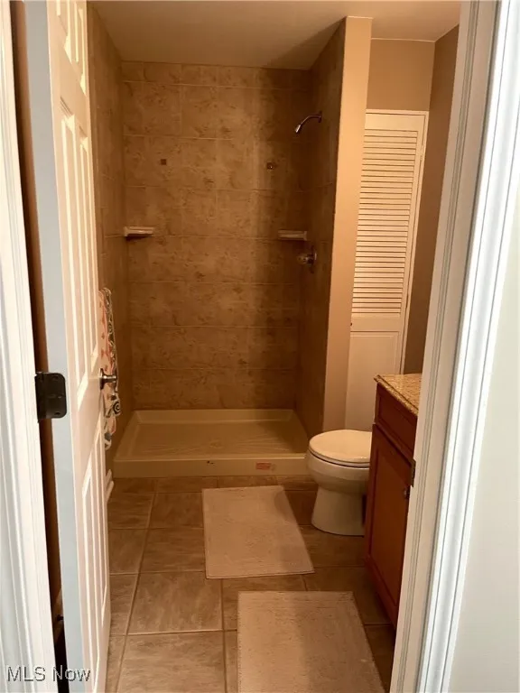 Bathroom with vanity, toilet, tile patterned floors, and a tile shower