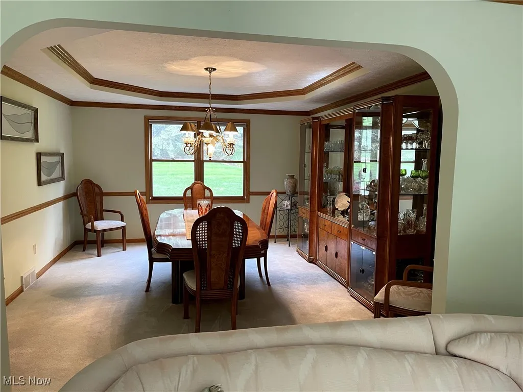 Dining space featuring a tray ceiling, arched walkways, crown molding, and light carpet