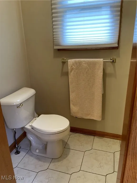 Half bathroom featuring toilet, marble look tile flooring, and baseboards