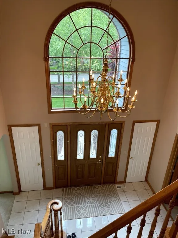 Foyer featuring a high ceiling, light tile patterned floors, a chandelier, and baseboards