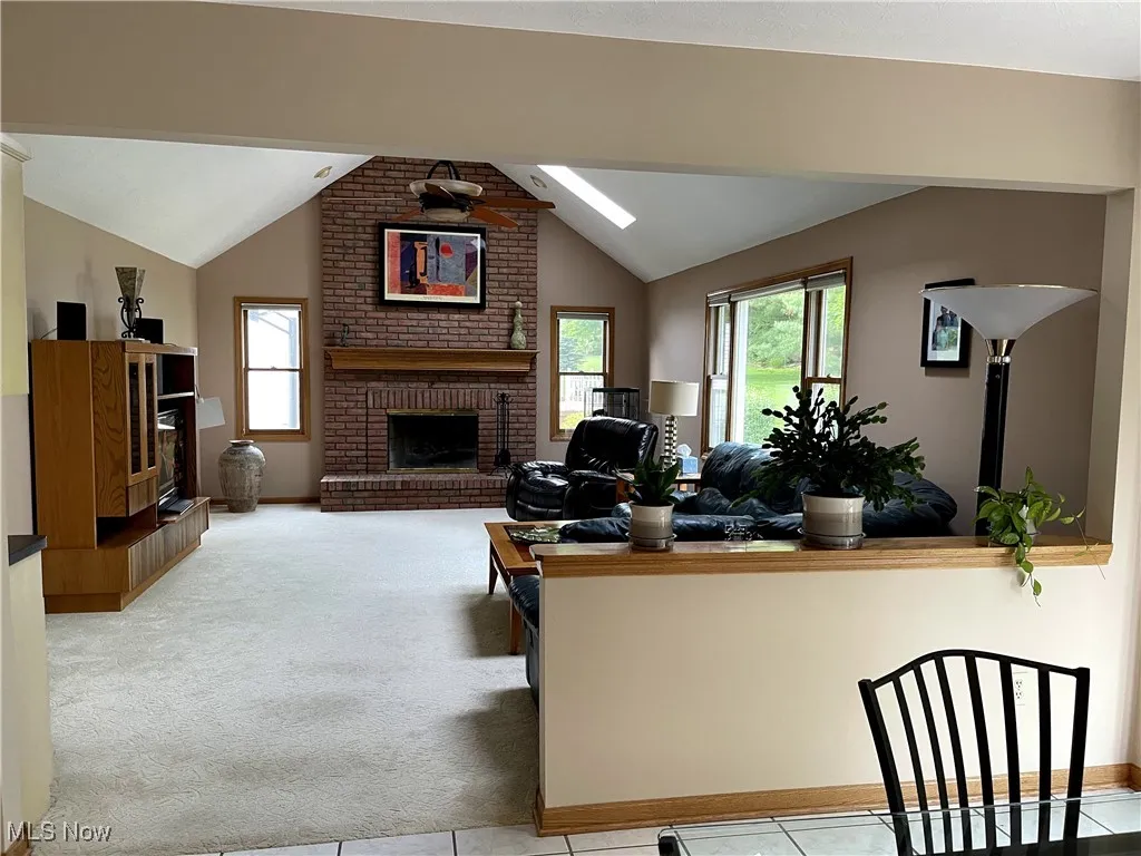 Carpeted living room with lofted ceiling, plenty of natural light, a brick fireplace, baseboards, and a skylight