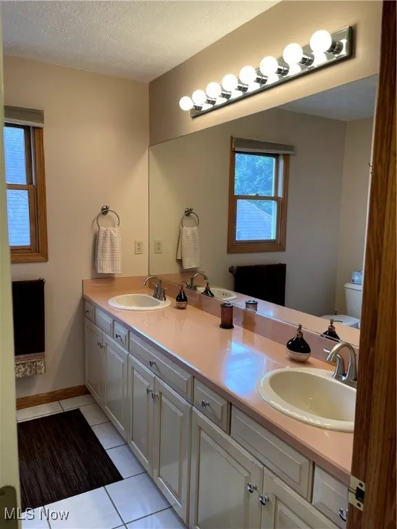 Bathroom featuring tile patterned floors, double vanity, toilet, and a textured ceiling