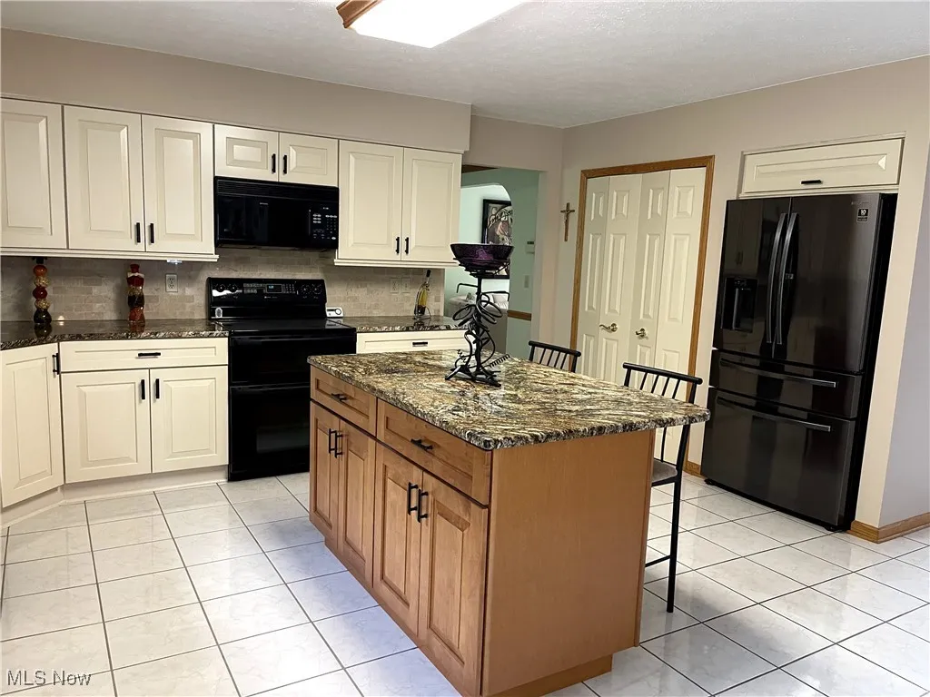 Kitchen with black appliances, a breakfast bar, dark stone counters, light tile patterned floors, and backsplash