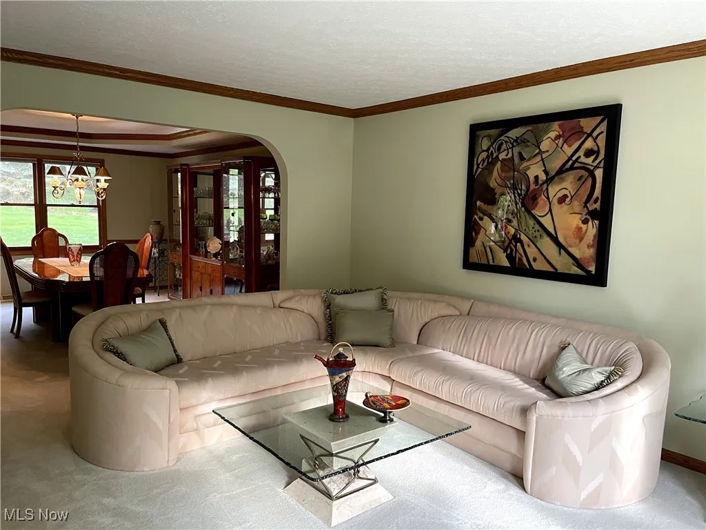 Living room featuring a chandelier, carpet floors, arched walkways, crown molding, and baseboards