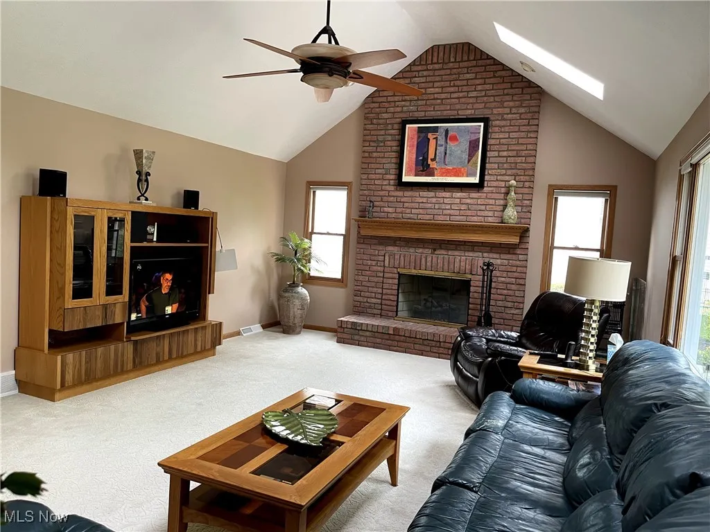 Carpeted living area featuring a brick fireplace, lofted ceiling, a ceiling fan, plenty of natural light, and baseboards