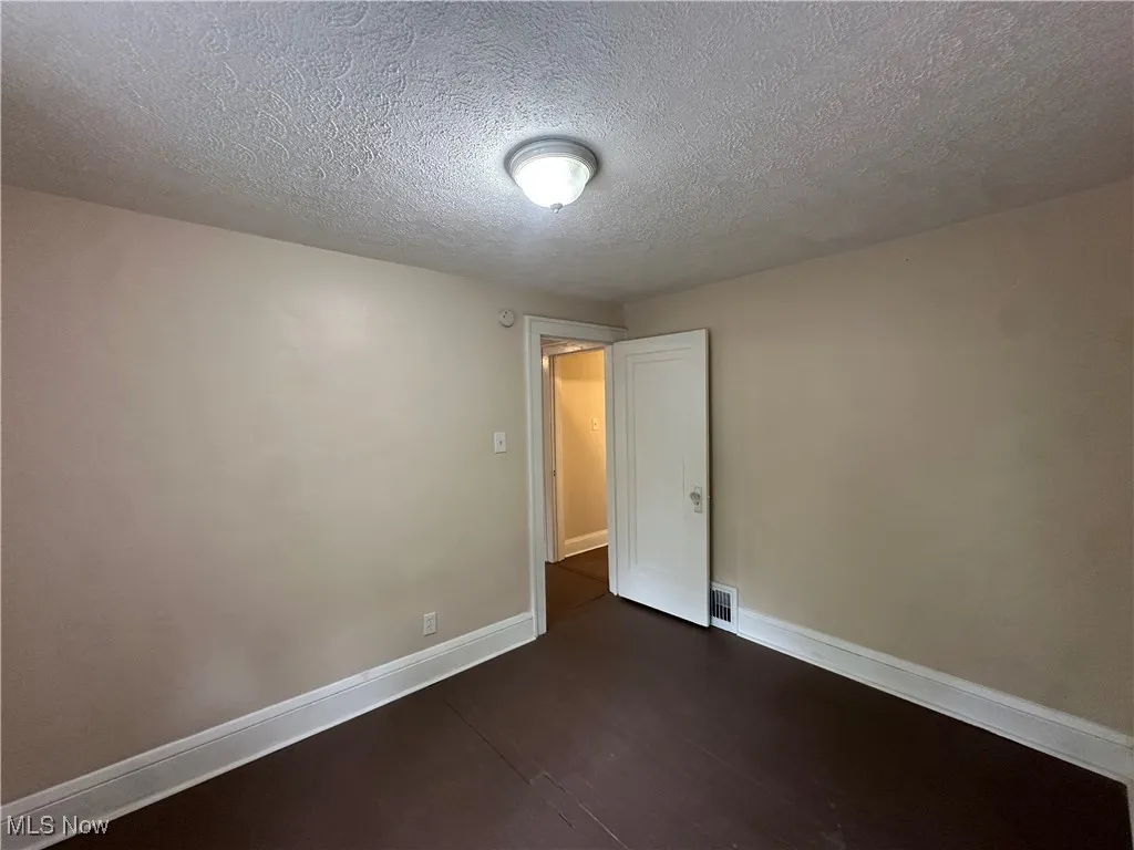 Empty room featuring dark wood-type flooring, baseboards, and a textured ceiling
