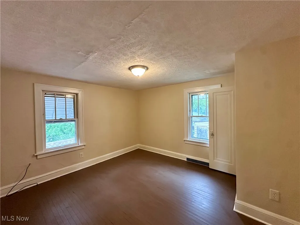 Unfurnished room featuring a textured ceiling, dark wood finished floors, and baseboards