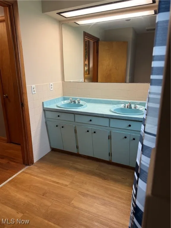 Full bathroom with tile walls, double vanity, wood finished floors, and wainscoting