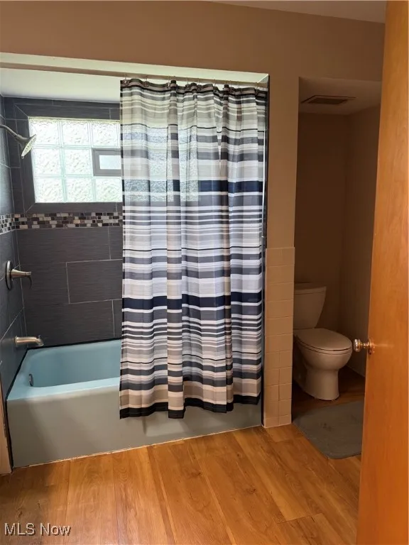 Bathroom with wood finished floors, toilet, and shower / tub combo with​​‌​​​​‌​​‌‌​‌‌​​​‌‌​‌​‌​‌​​​‌​​ curtain