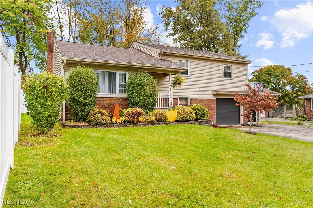 Split level home featuring concrete driveway, a garage, a chimney, brick siding, and a front lawn