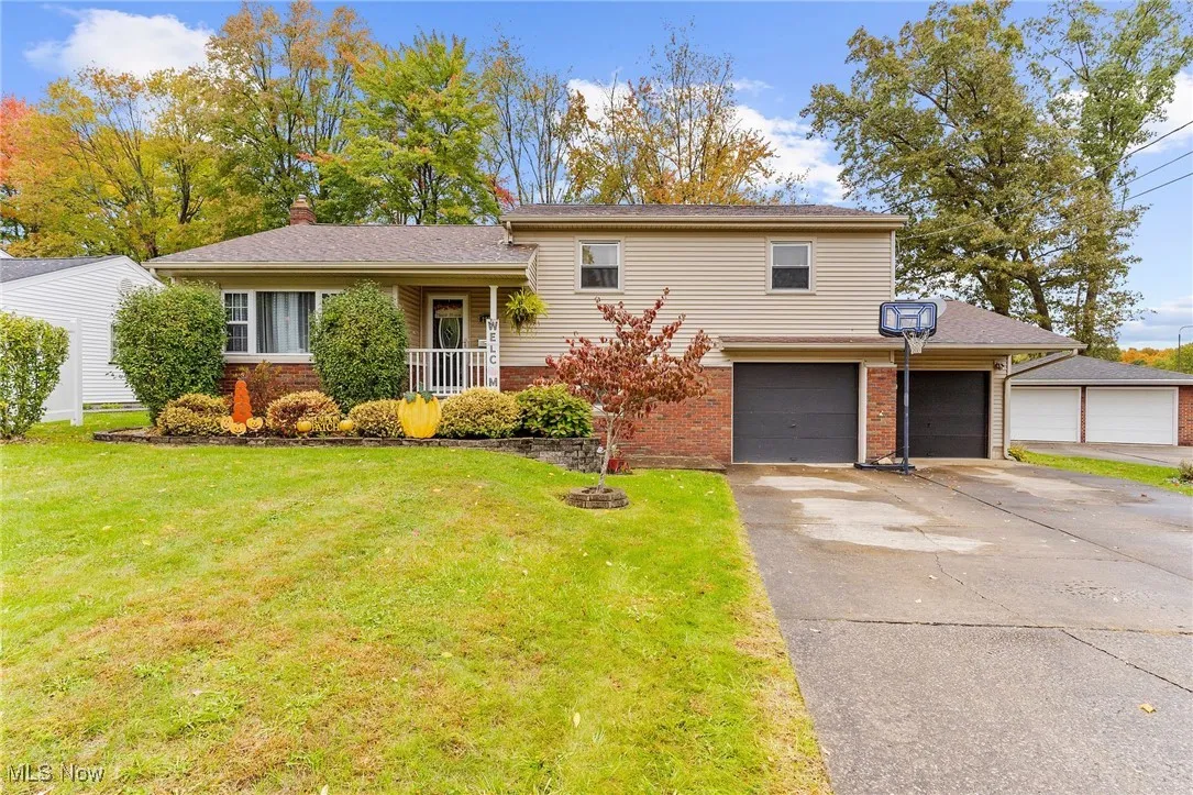 Tri-level home featuring a front yard, a chimney, brick siding, concrete driveway, and a garage