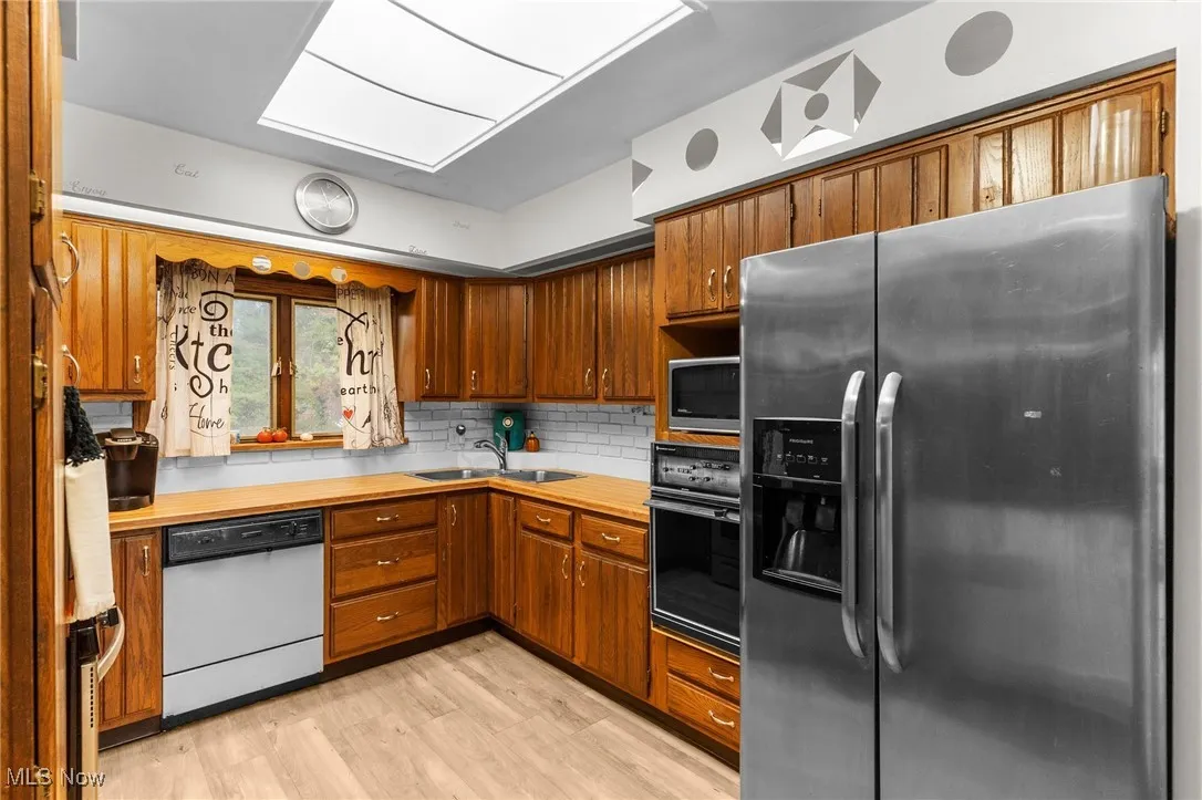 Kitchen with appliances with stainless steel finishes, a sink, light countertops, and brown cabinetry