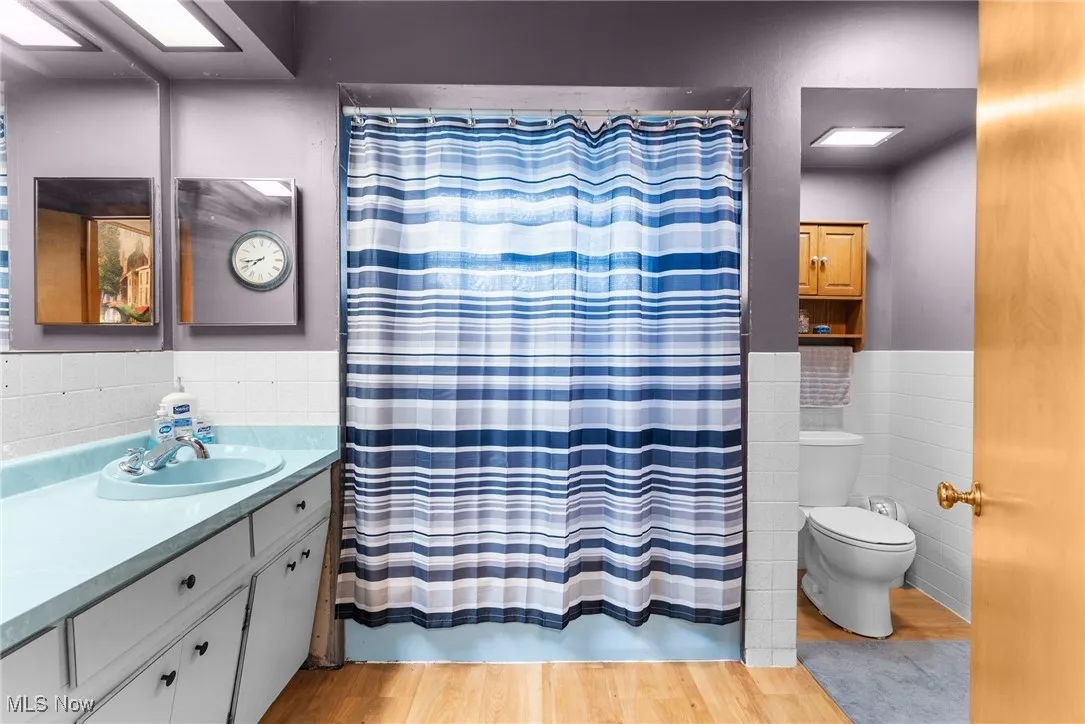 Full bath featuring tile walls, toilet, vanity, a wainscoted wall, and wood finished floors