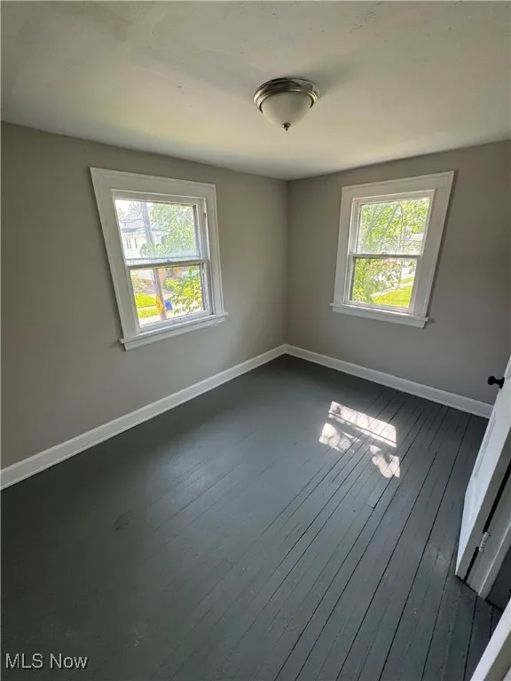 Unfurnished room with dark wood-type flooring, plenty of natural light, and baseboards