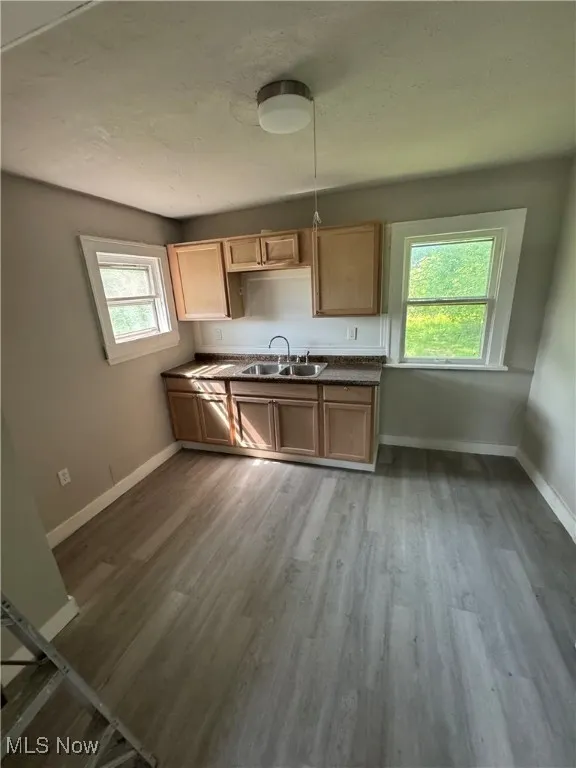 Kitchen featuring a sink, baseboards, wood finished floors, dark countertops, and a textured ceiling