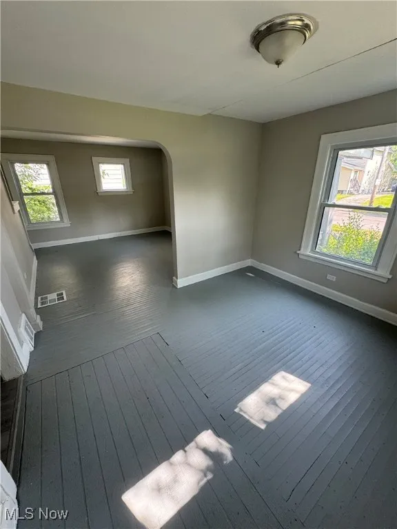 Spare room featuring dark wood-type flooring, baseboards, and arched walkways