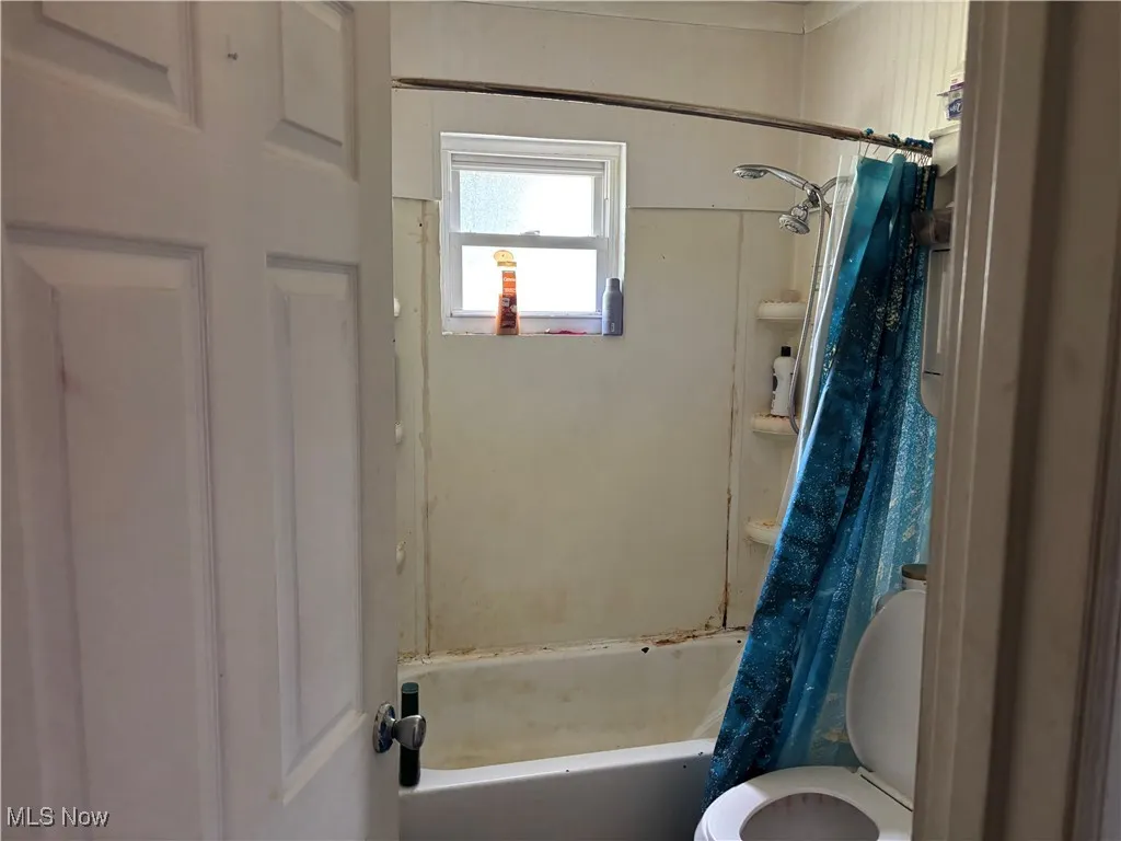 Bathroom featuring toilet and shower / bath combination with curtain