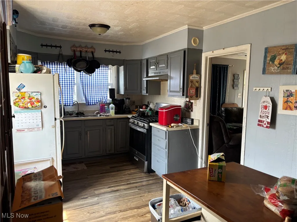 Kitchen with freestanding refrigerator, gray cabinets, gas stove, a sink, and light wood-type flooring