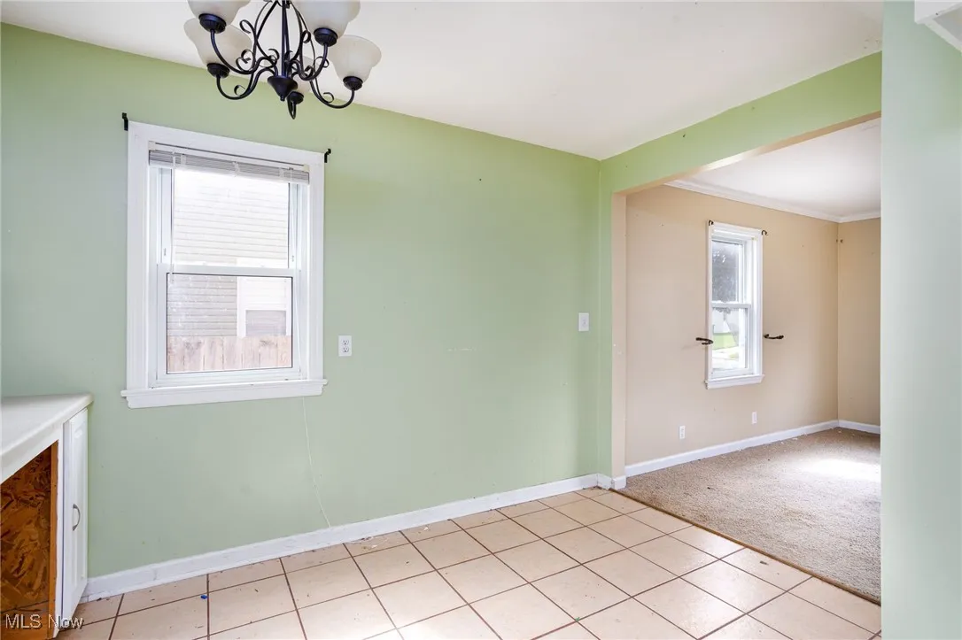 Unfurnished dining area with baseboards, a chandelier, light carpet, and light tile patterned flooring