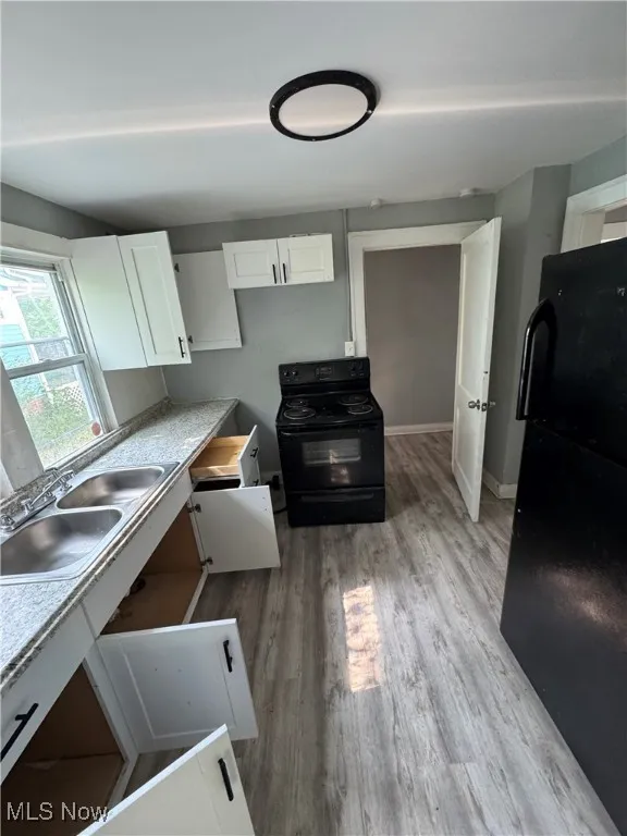 Kitchen with black appliances, a sink, white cabinetry, light wood-type flooring, and baseboards