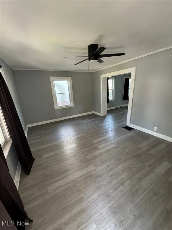 Spare room with a ceiling fan, baseboards, dark wood-style flooring, and ornamental molding