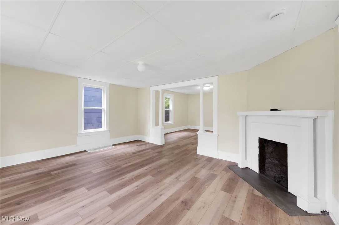 Unfurnished living room with light wood-type flooring, a fireplace with raised hearth, and baseboards