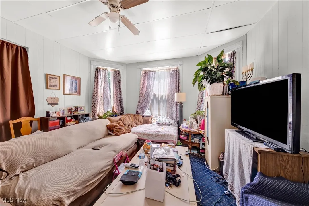 Living area featuring ceiling fan, wooden walls, and carpet