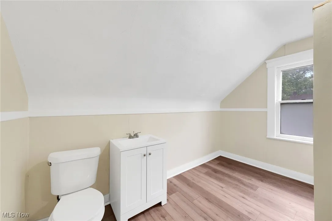 Half bathroom with toilet, wood finished floors, lofted ceiling, vanity, and baseboards
