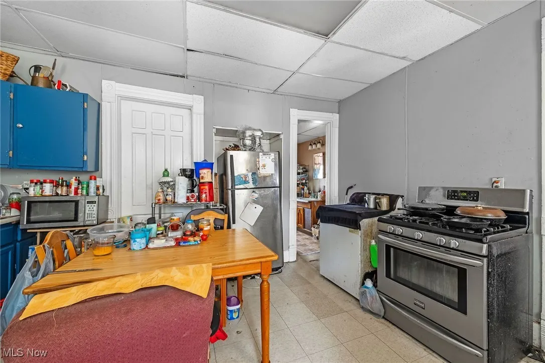 Kitchen featuring stainless steel appliances, blue cabinetry, a drop ceiling, and light floors
