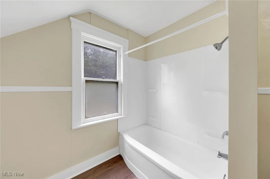 Full bath featuring wood finished floors, shower / bathtub combination, baseboards, and vaulted ceiling