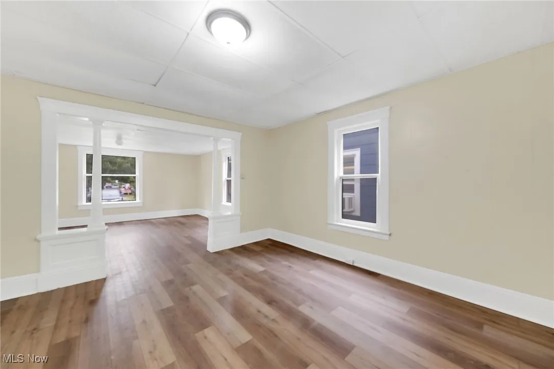 Empty room with wood finished floors, baseboards, and decorative columns