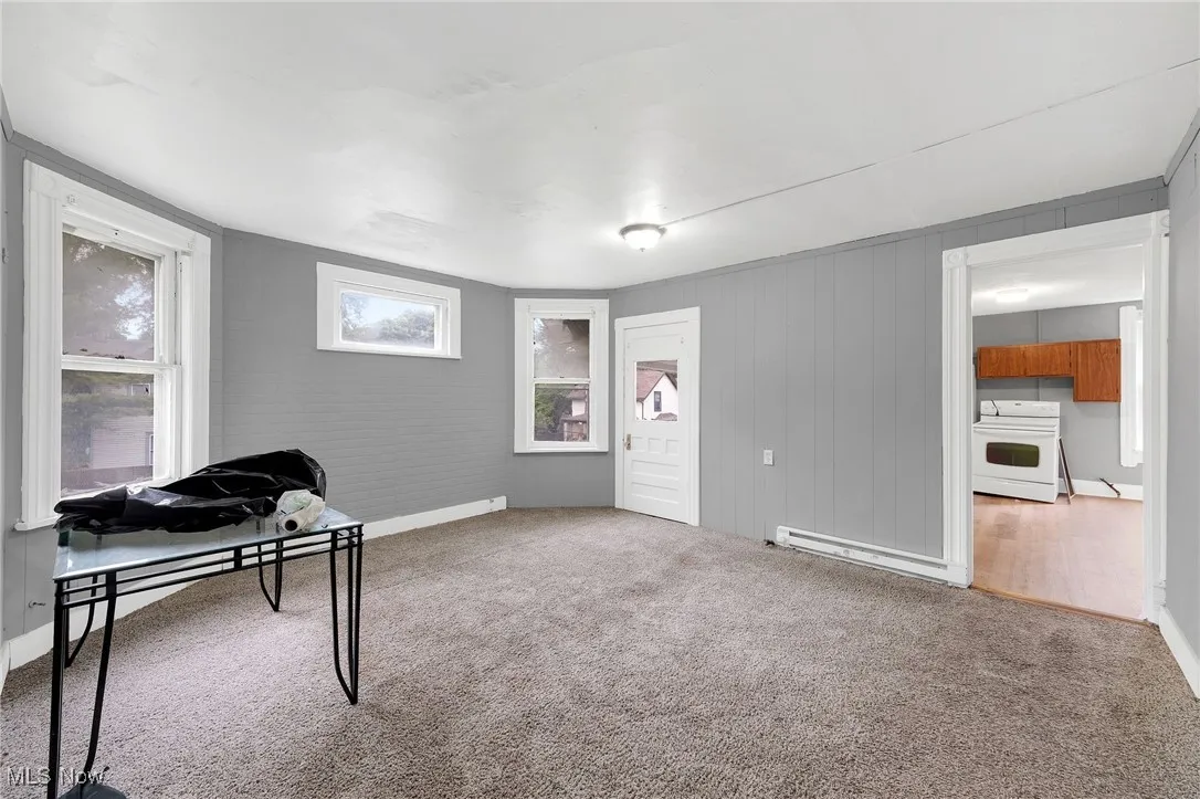 Carpeted office space featuring a baseboard radiator and baseboards